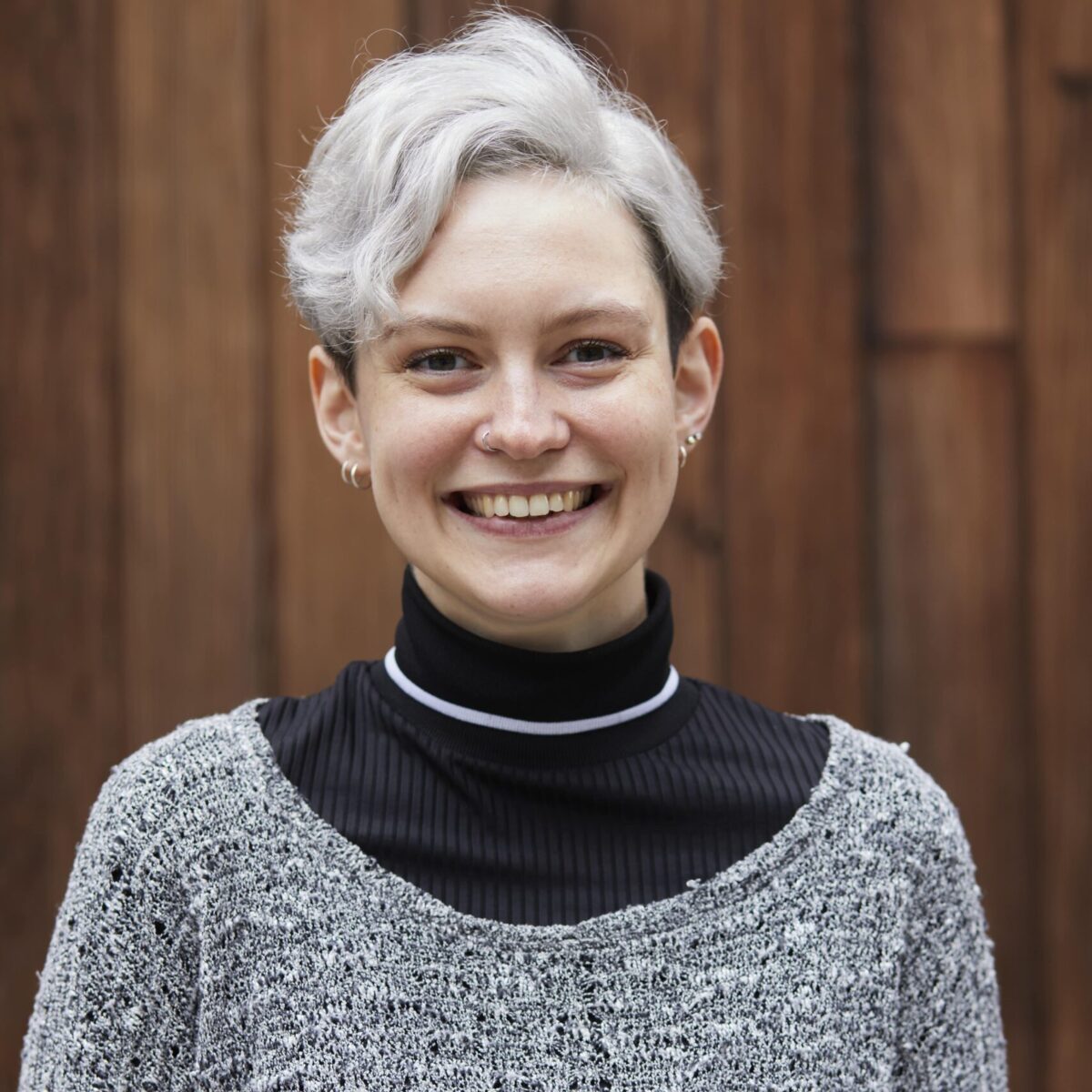 A profile shot of designer Anna Reid, Ana wears a black polo top underneath a grey cardigan and silver necklace. She smiles directly into the camera